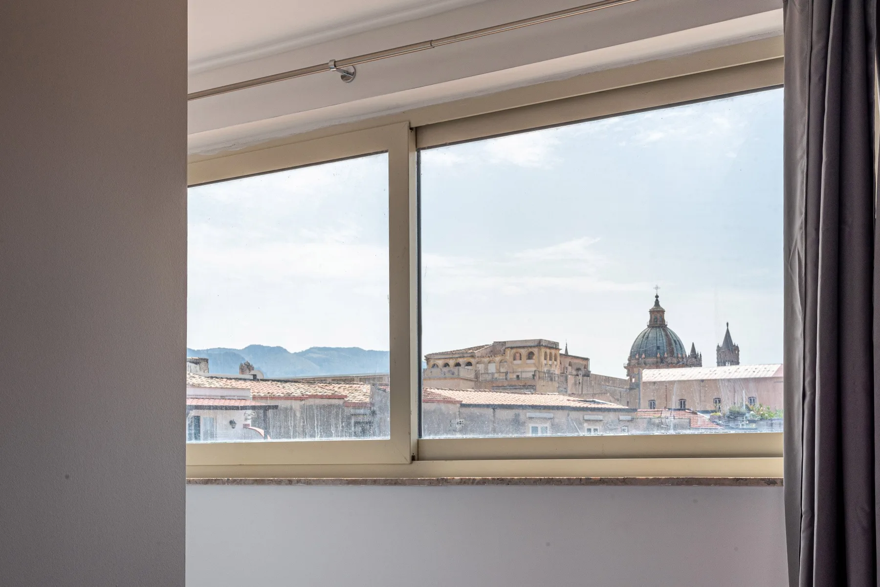 A wide window overlooks city rooftops and a domed building.