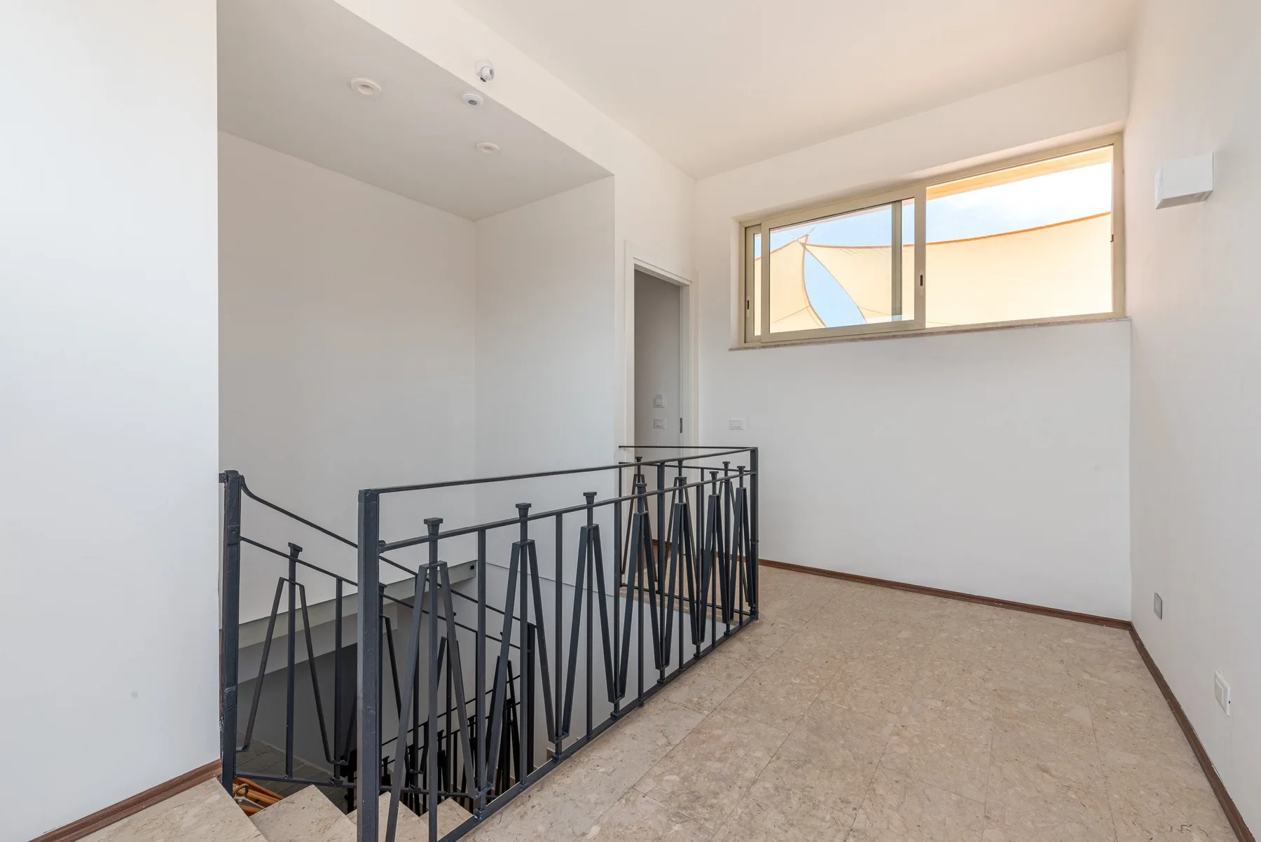 A bright interior landing with a black metal railing and a high window.