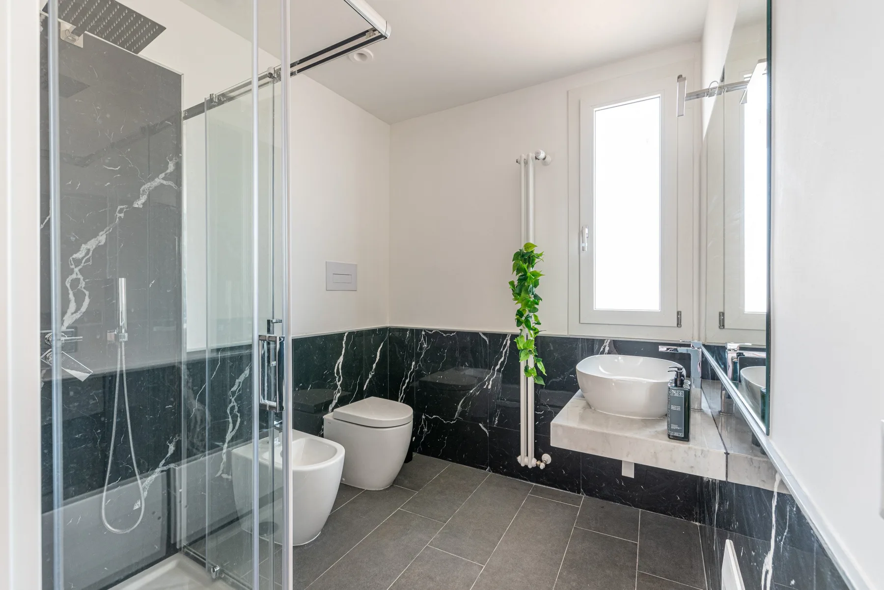 A modern bathroom with a glass shower and a sink beneath the window.