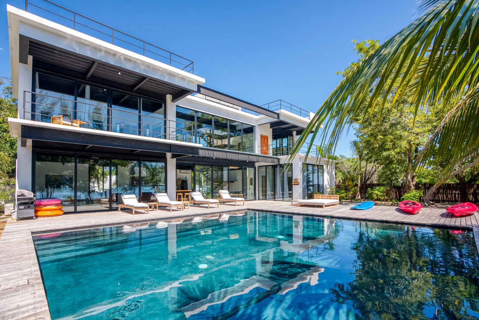 A modern glass-fronted house overlooks a swimming pool and wooden deck.
