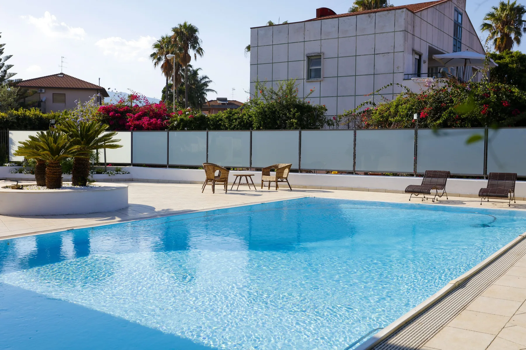 An outdoor swimming pool with patio seating and landscaped greenery.