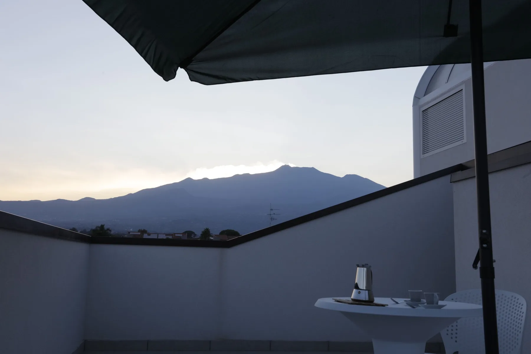 A rooftop terrace with a table and mountain views at dusk.