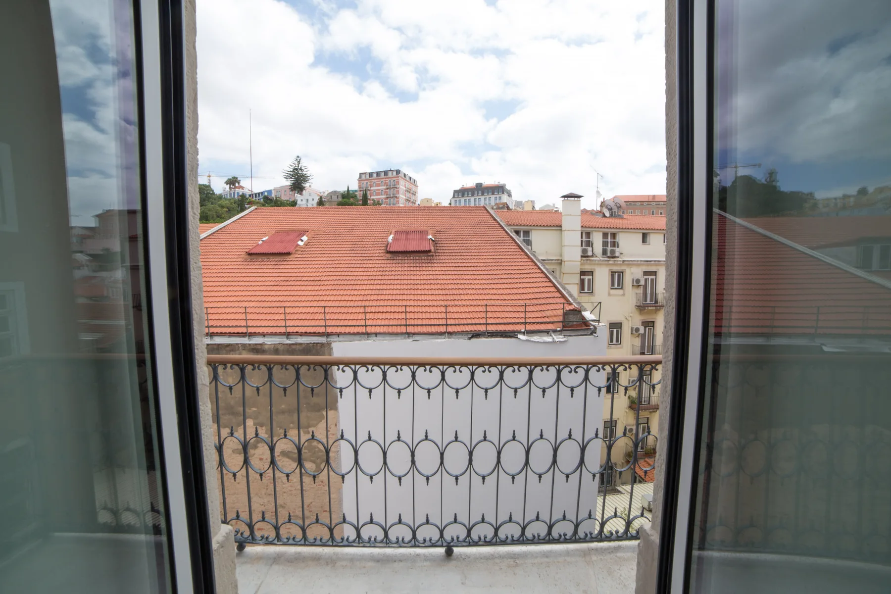 Vista de la ciudad desde una ventana abierta, con tejados cercanos y una barandilla de balcón.