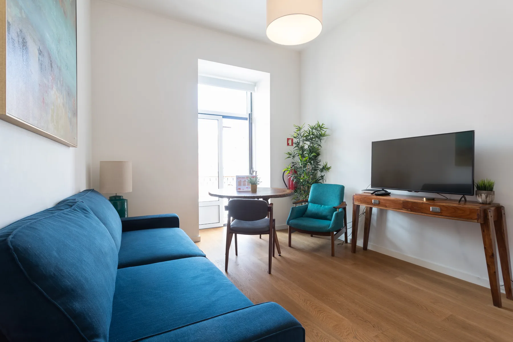 Una sala luminosa con asientos azules, un televisor y una pequeña zona de comedor.