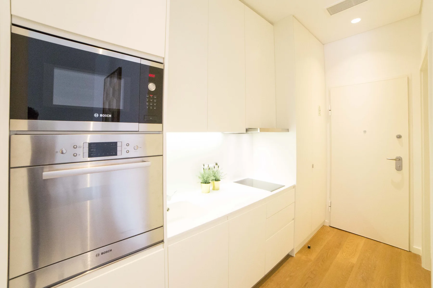 Una cocina pequeña y luminosa con electrodomésticos integrados y armarios blancos.