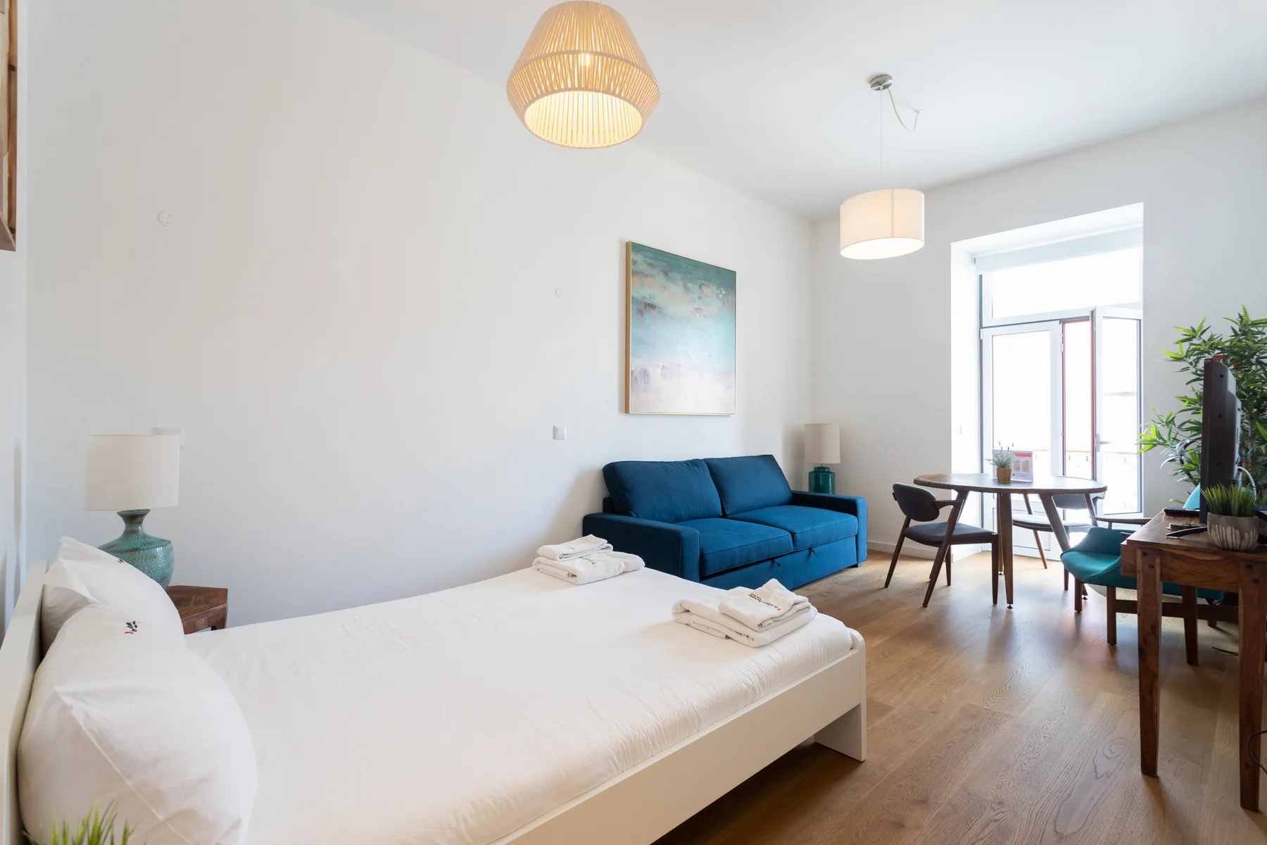 Estudio con cama, asientos azules y una mesa de comedor junto a la ventana.