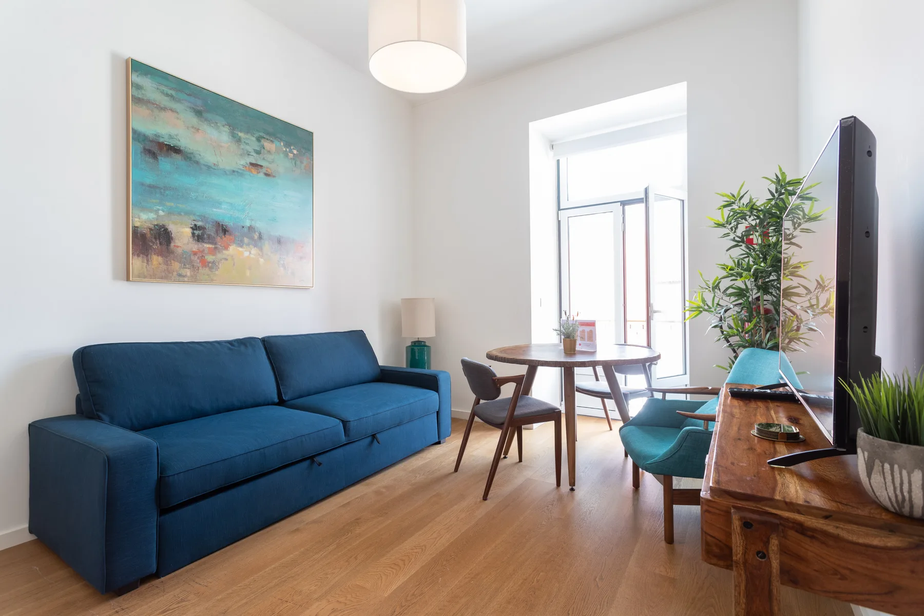 Una sala luminosa con asientos azules, una mesa de comedor y ventanas grandes.