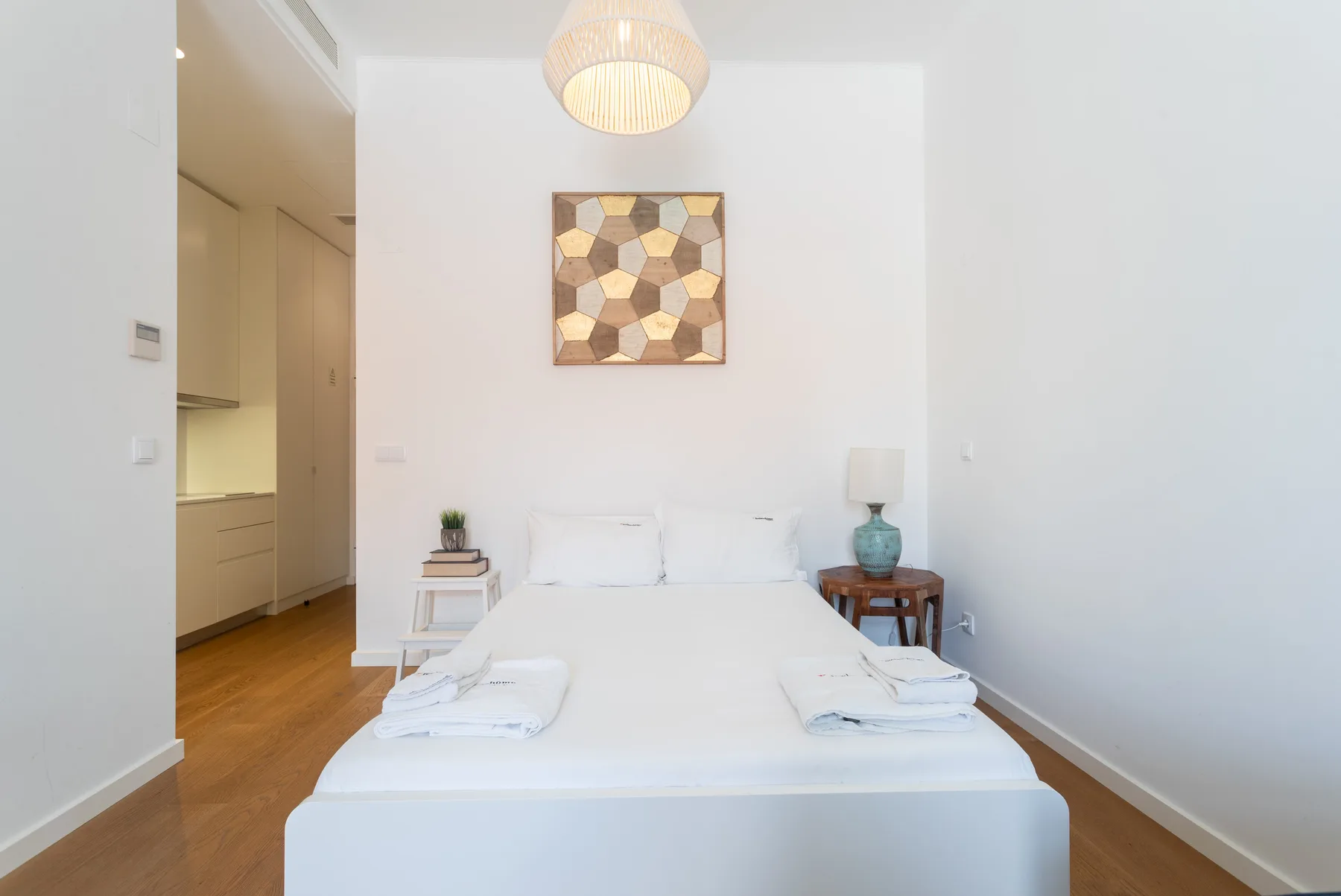 Un dormitorio luminoso con una cama bien hecha y arte geométrico en la pared.