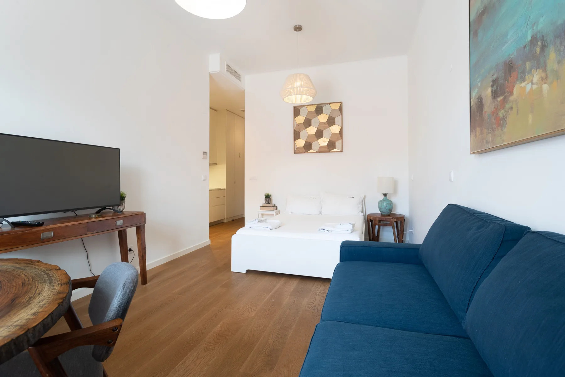 Una sala luminosa con un sofá azul, un televisor y una cama.