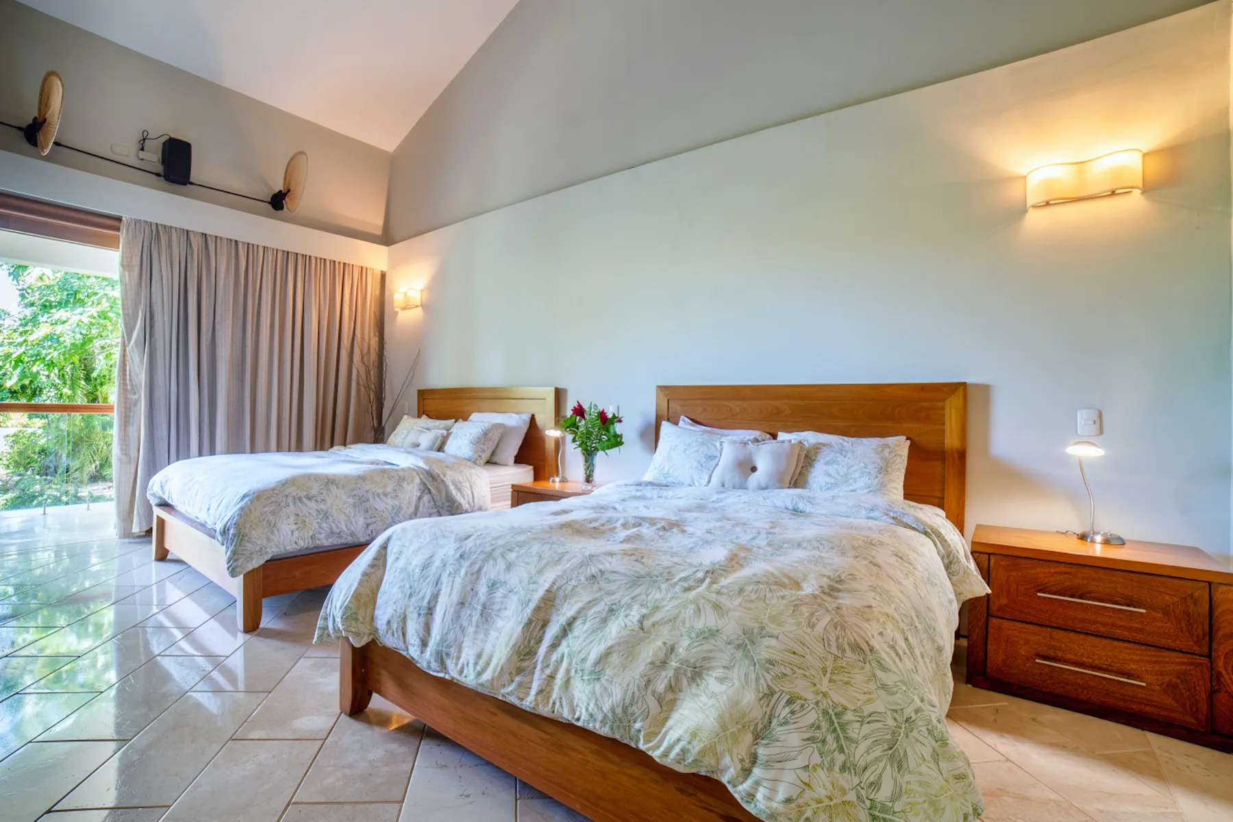 Dormitorio con dos camas, mesitas de noche y una puerta de vidrio con cortinas.