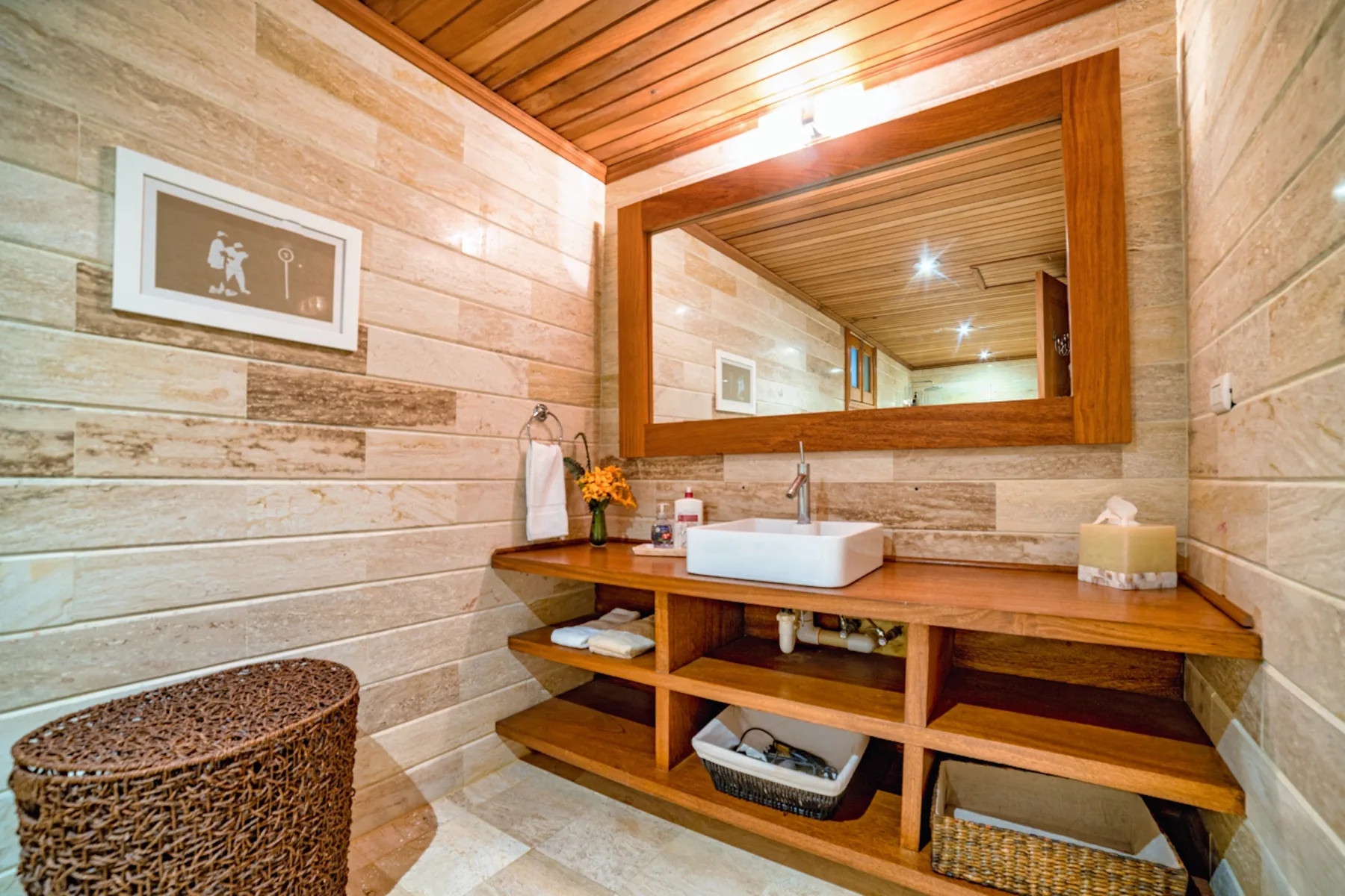 Un tocador de baño con un espejo grande, una encimera de madera y una cesta tejida.