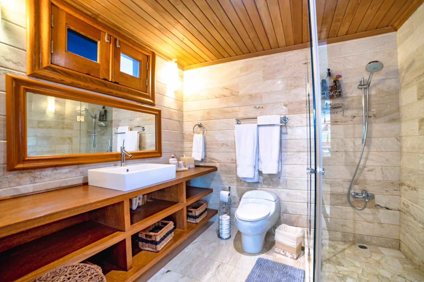 Un baño con mueble de madera, lavabo, inodoro y ducha de vidrio.