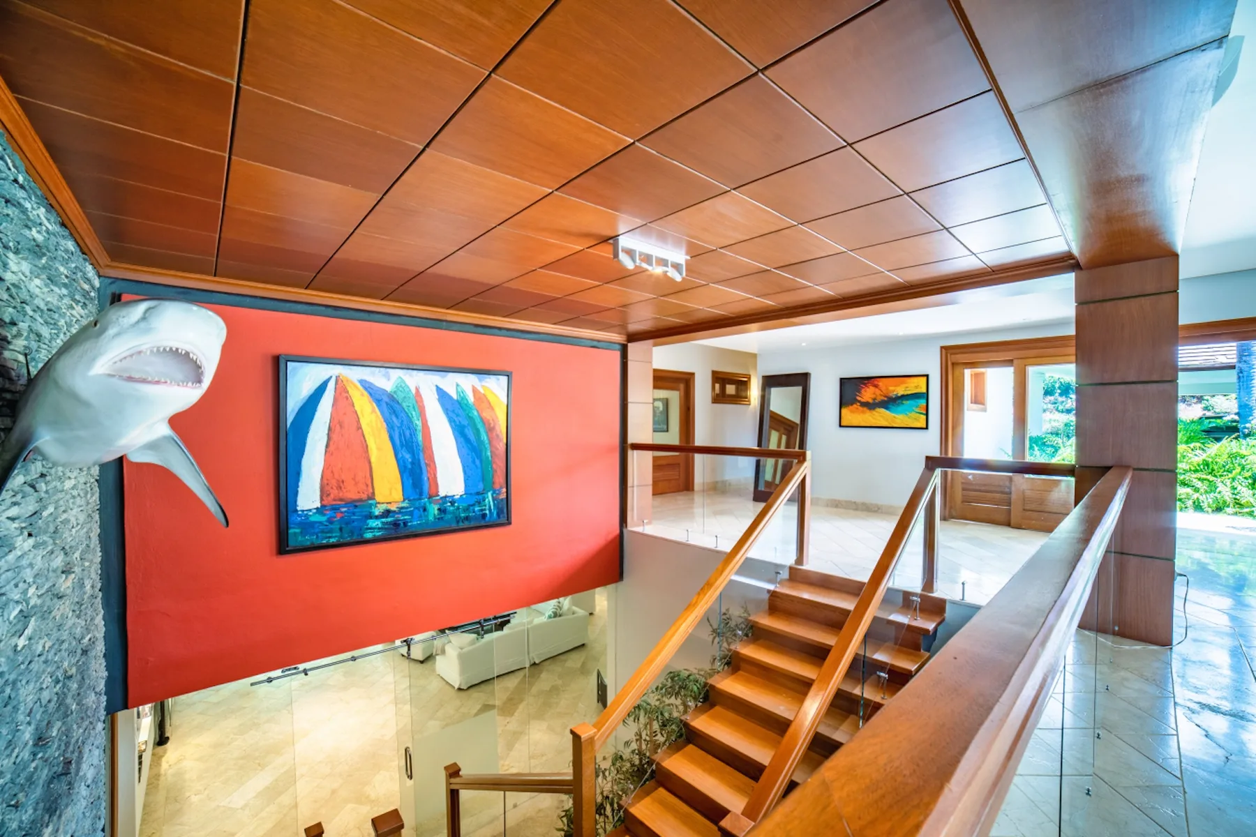 Un rellano interior luminoso tiene una escalera de madera junto a coloridas obras de arte.