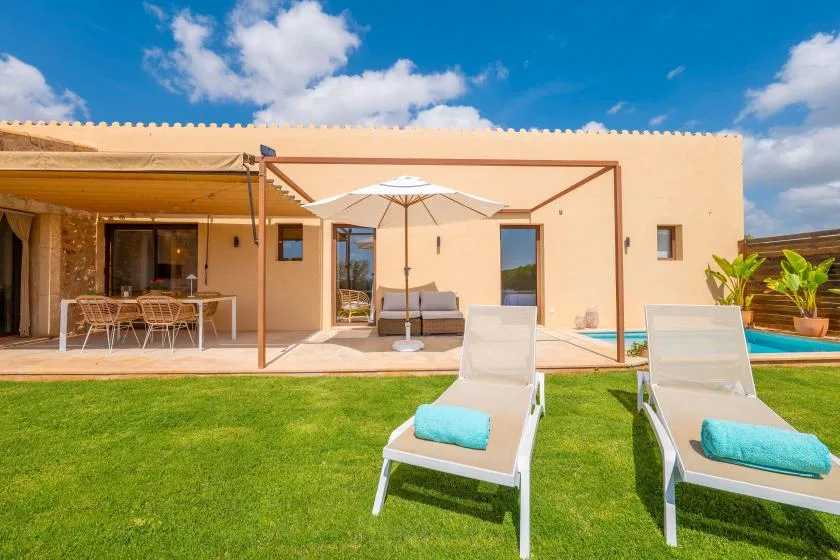 A sunny patio and lawn in front of a house, with outdoor seating and an umbrella.