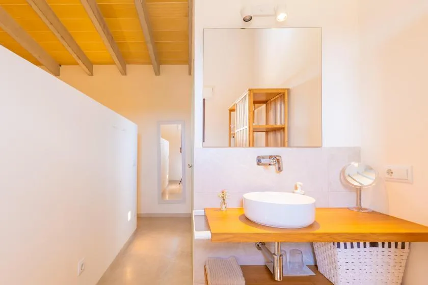 A bright bathroom with a round basin set on a wooden vanity beneath a large mirror.