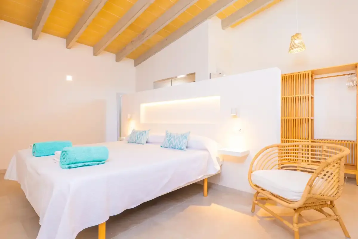 A bright bedroom with a white bed, turquoise towels, and a wicker chair.
