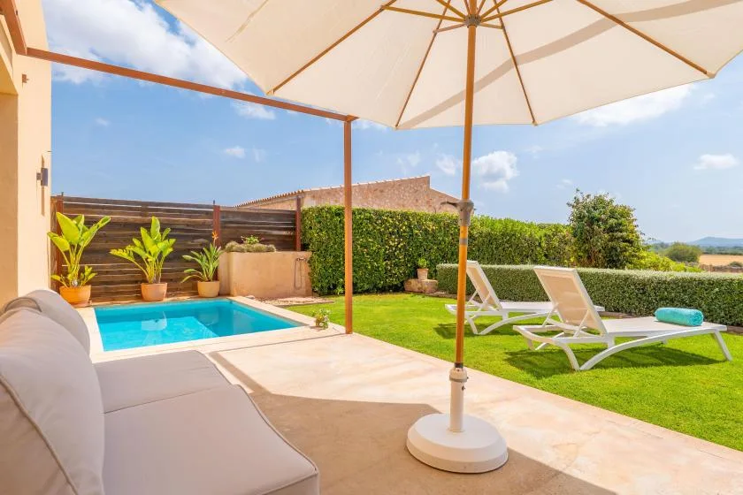 A sunny outdoor patio with a swimming pool, seating, and a large umbrella.