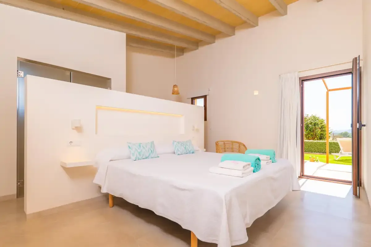 A bright bedroom with a neatly made bed and open doors to the garden.