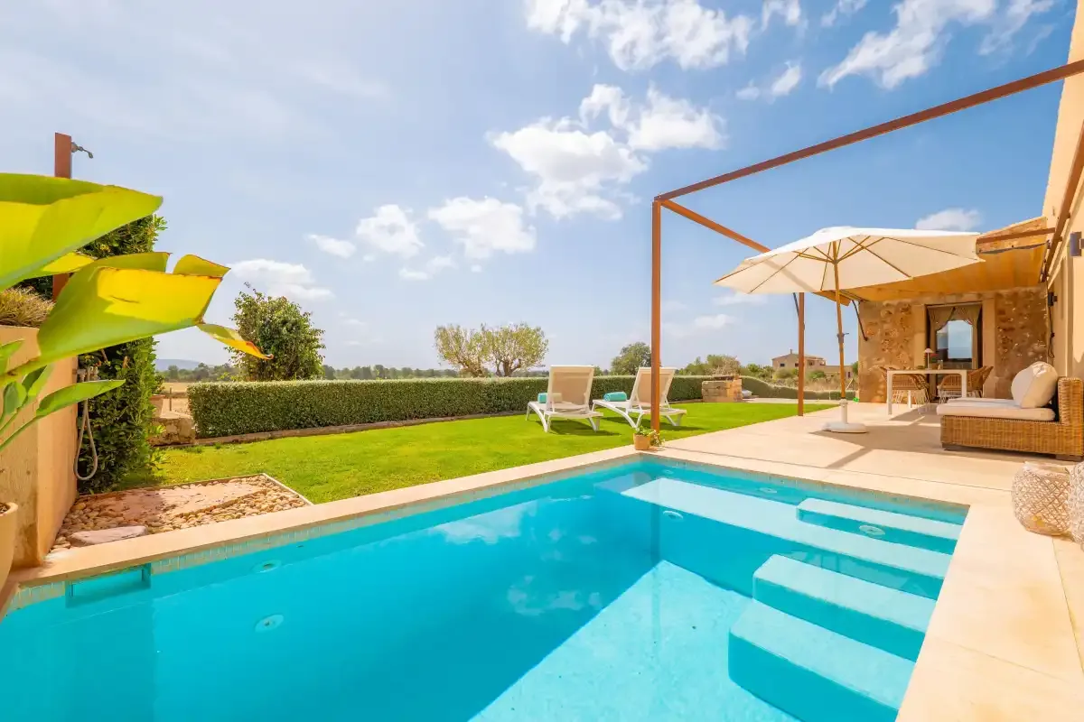 A swimming pool beside a lawn and a shaded outdoor seating area.