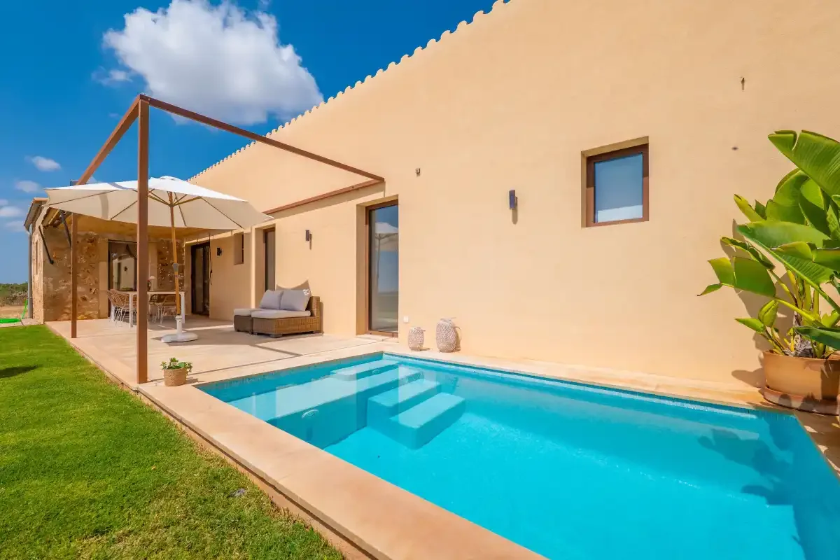 A swimming pool beside a pale exterior wall and shaded patio.