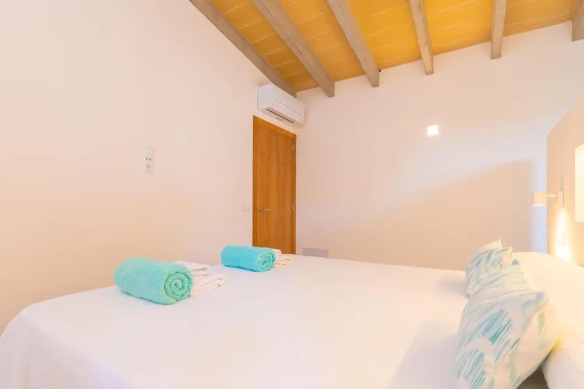 A bedroom with a white bed and exposed wooden ceiling beams.