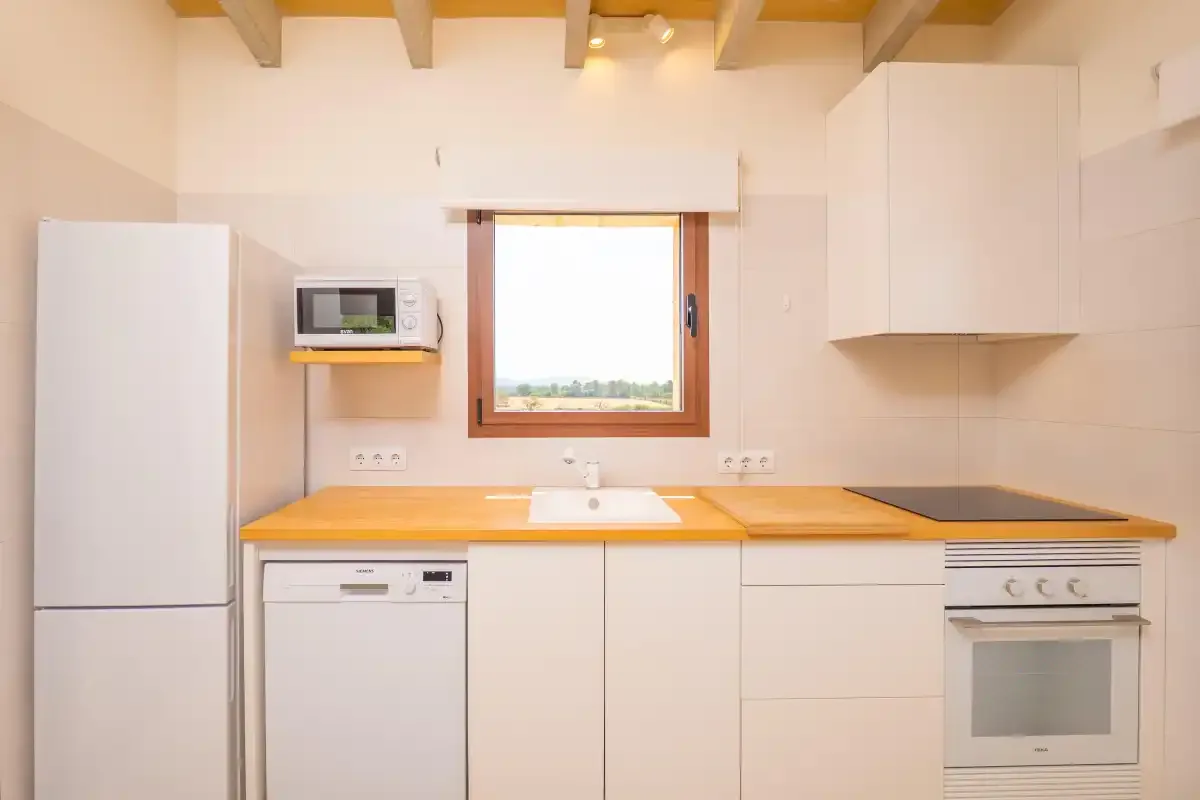 A bright kitchen with white cabinets, a wooden countertop, and a window.
