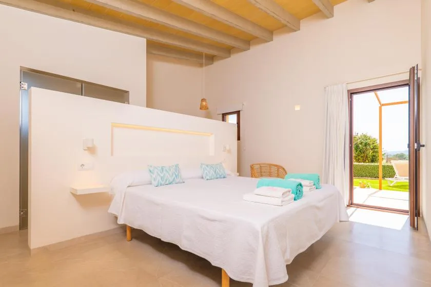 A bright bedroom with a white bed and an open glass door to the garden.
