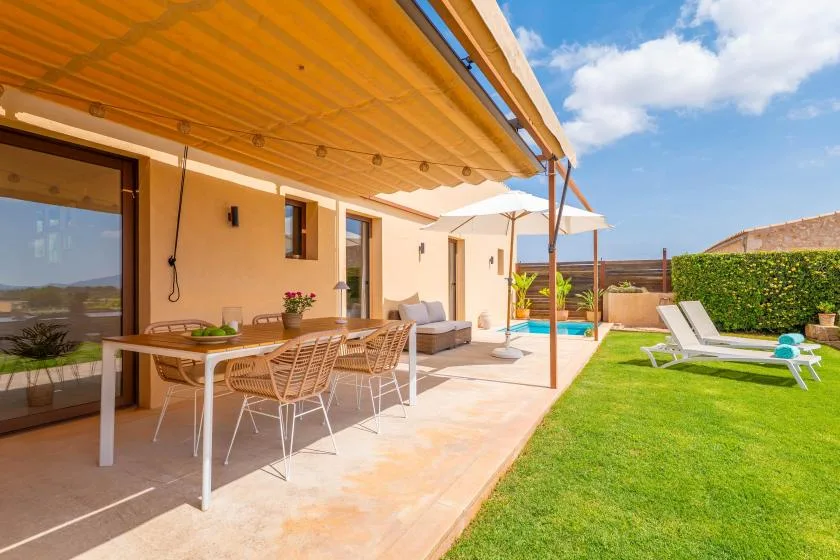 A covered patio with outdoor dining seating opens onto a lawn and small pool.