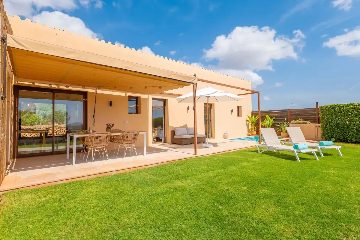A modern house opens onto a patio with outdoor seating and a lawn.