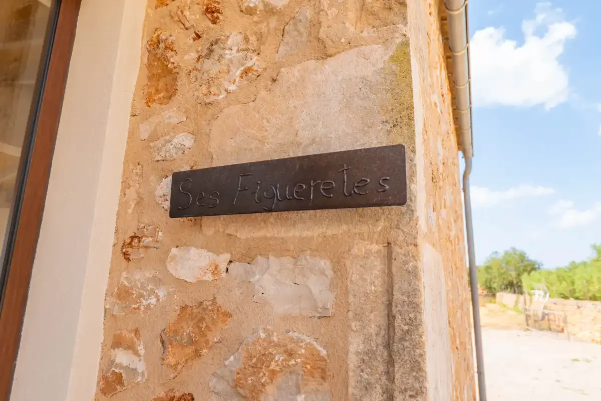 A stone exterior wall displays a dark plaque beside a sunlit path.