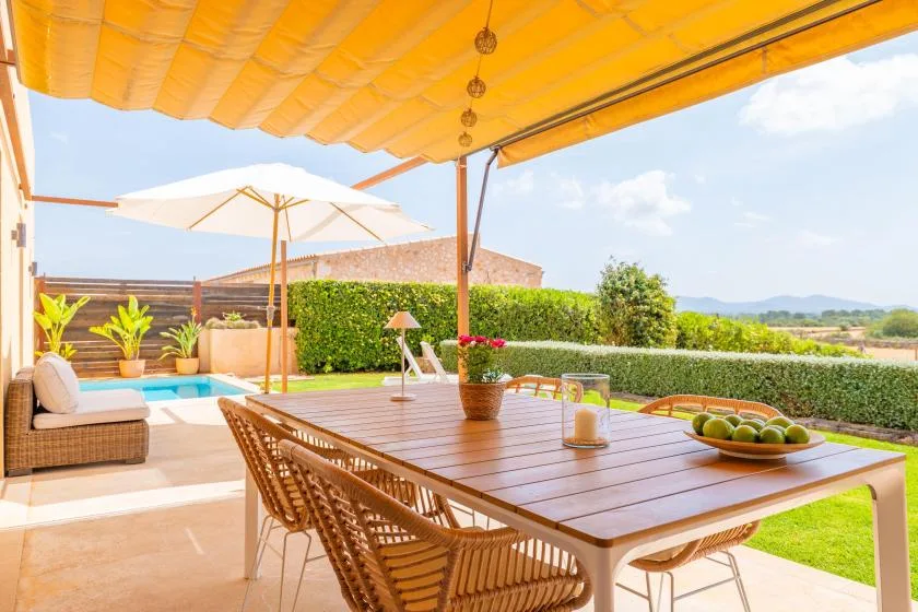 A shaded outdoor dining area with a large table overlooking a garden.