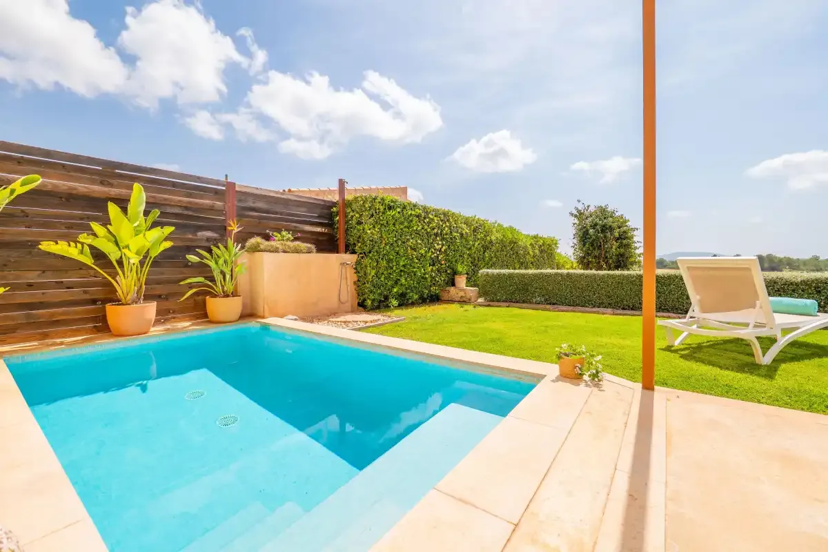 An outdoor swimming pool beside a lawn, potted plants, and a reclining chair.