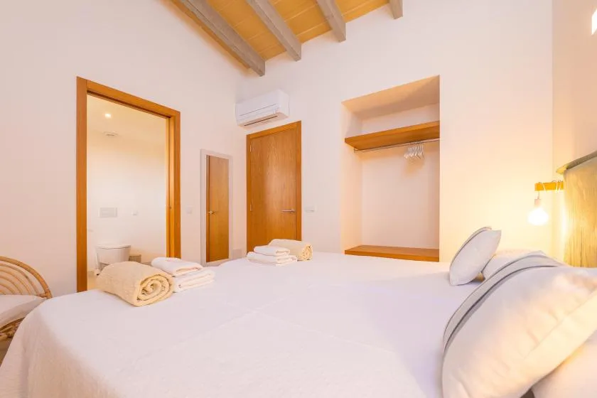 A bright bedroom with a neatly made bed and wooden ceiling beams.