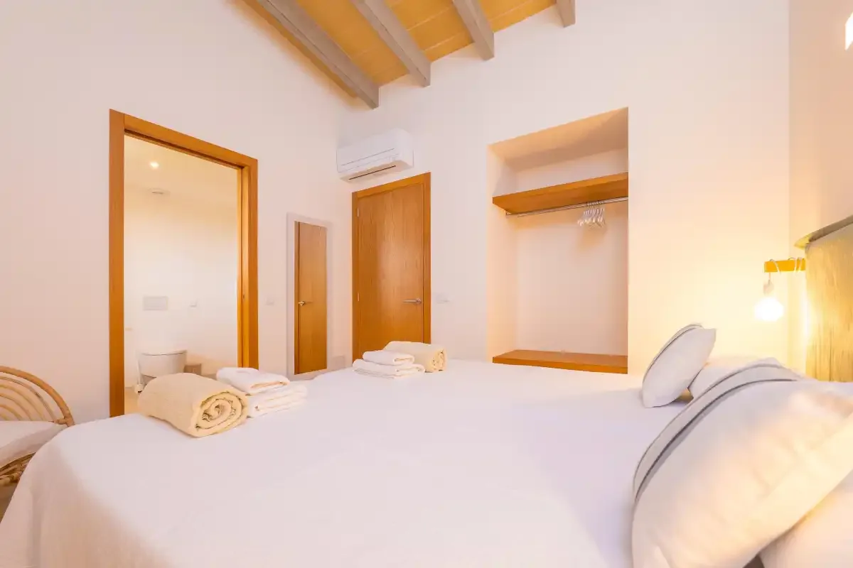 A bright bedroom with a bed, exposed ceiling beams, and a recessed clothes rail.