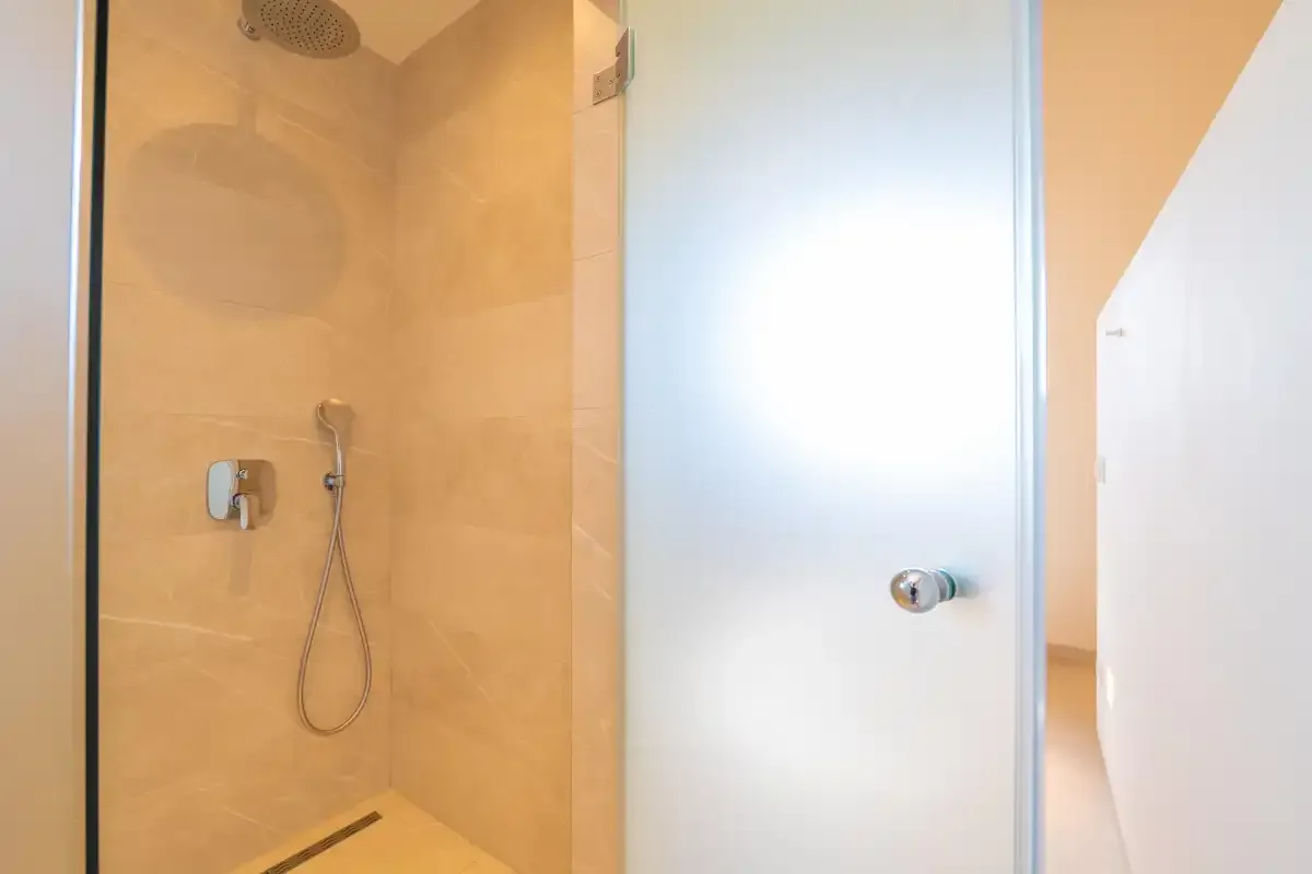 A tiled shower area with a handheld shower fixture beside a frosted glass panel.