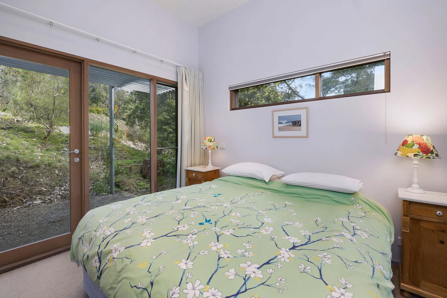 A bedroom with a bed and sliding glass doors overlooking greenery.