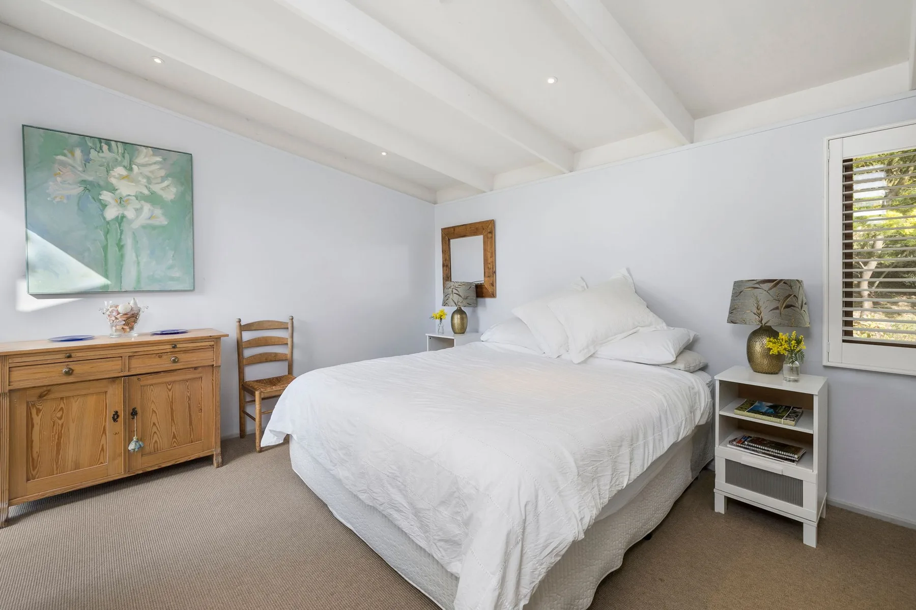 A bright bedroom with a neatly made bed, wooden dresser, and window.