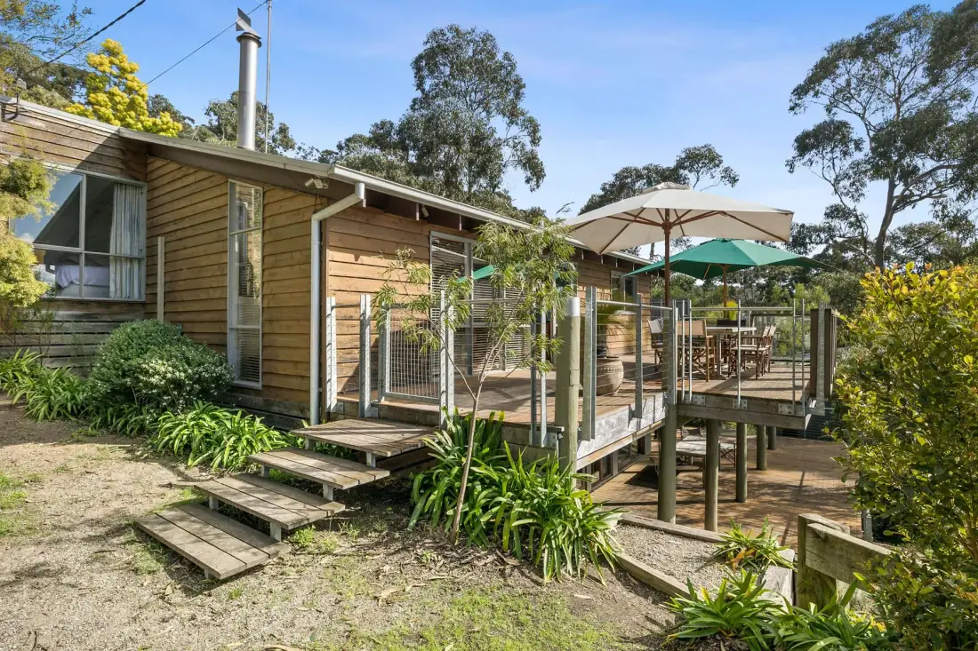 A wooden cabin with a raised deck, outdoor seating, and umbrellas.