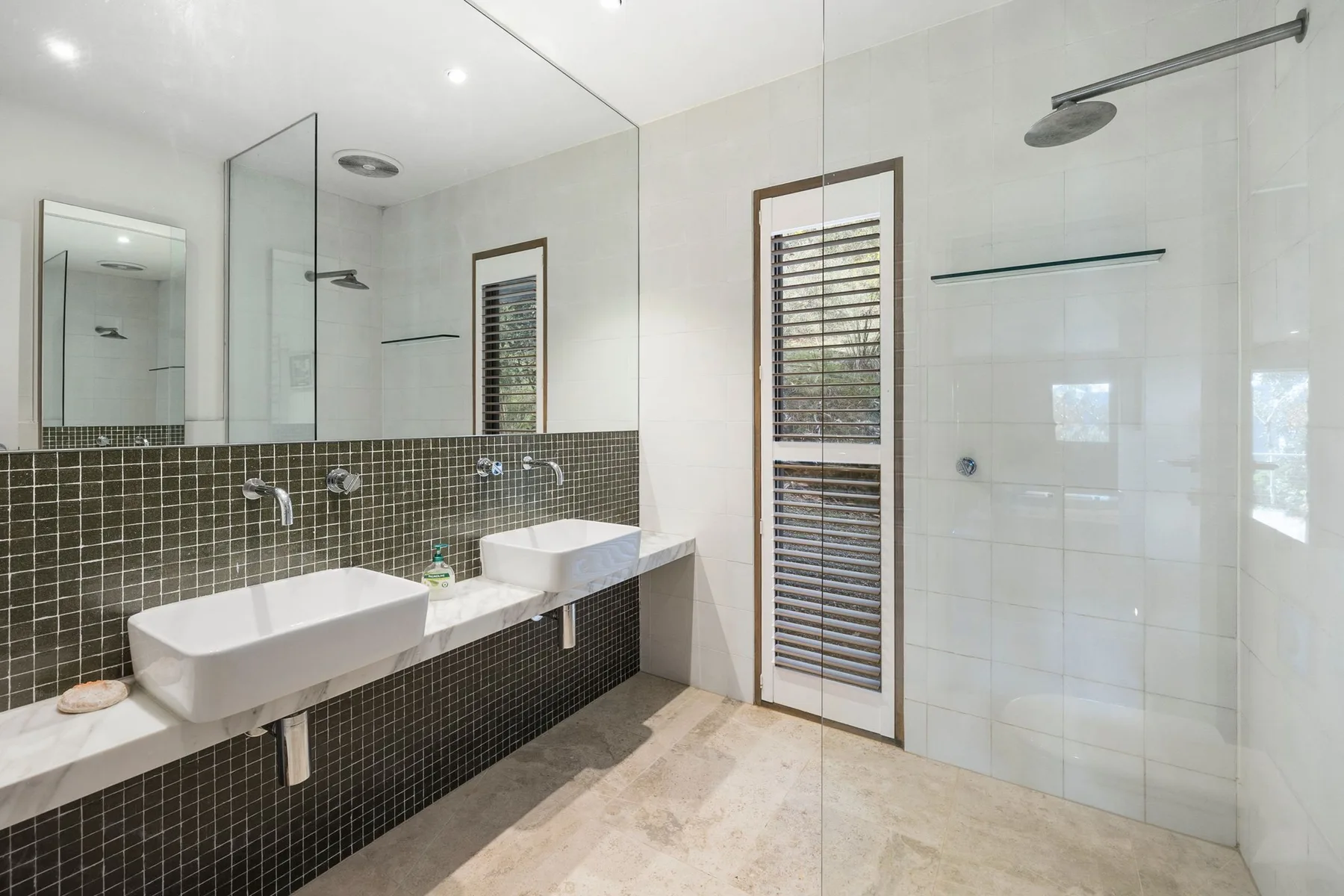 A bright bathroom with a long vanity and glass-enclosed shower.