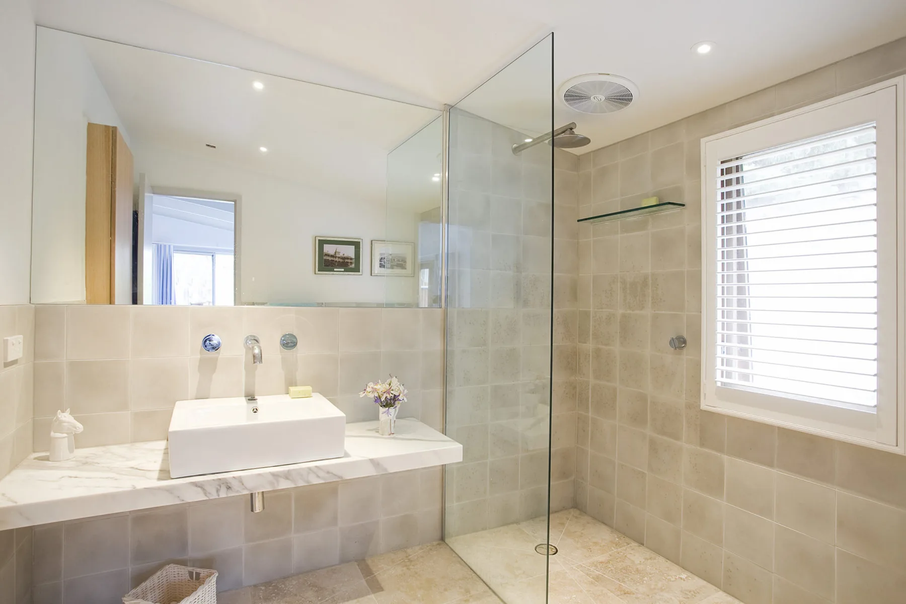 A bright bathroom with a wide mirror, a vanity, and a glass shower.