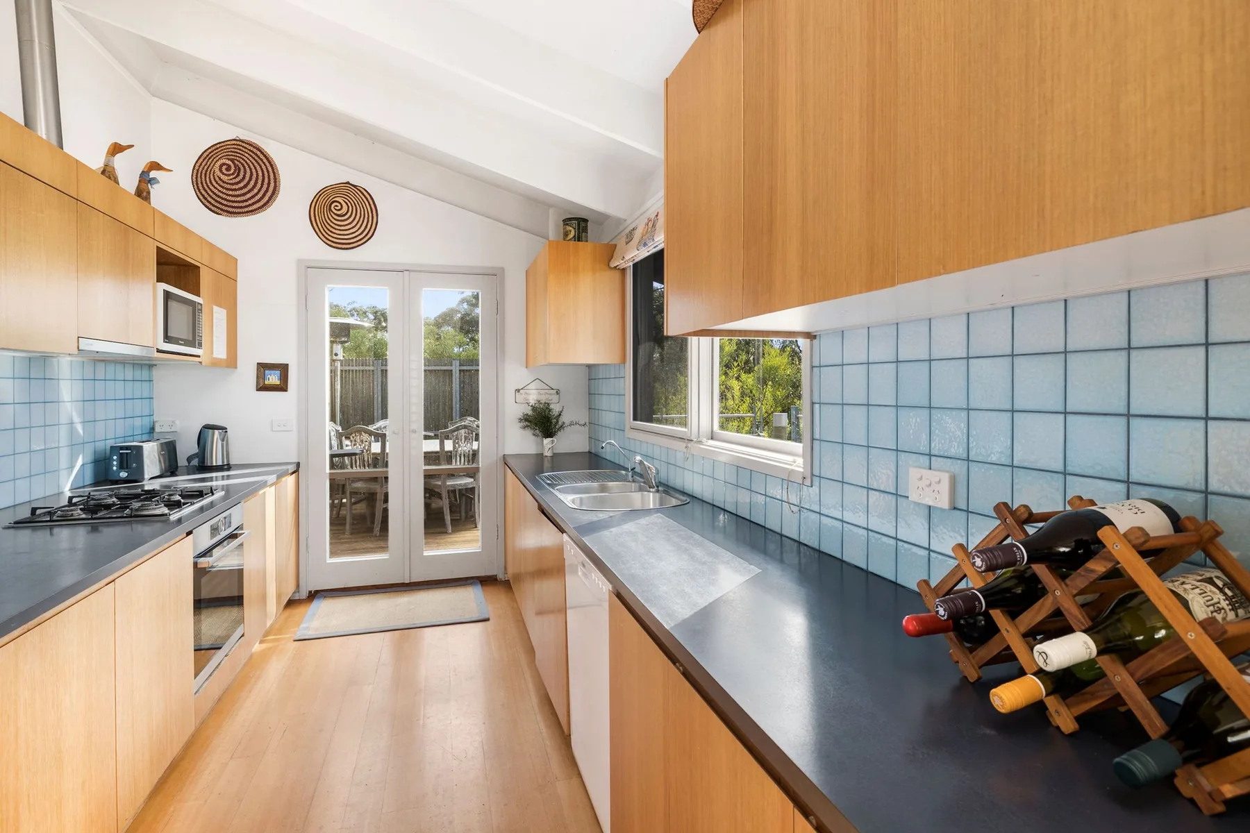 A bright kitchen with wooden cabinets, blue tile, and a central passage.