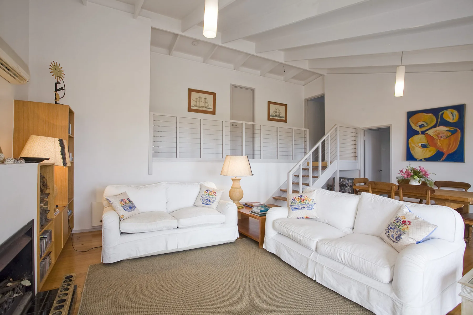A bright living room with white seating and a staircase.