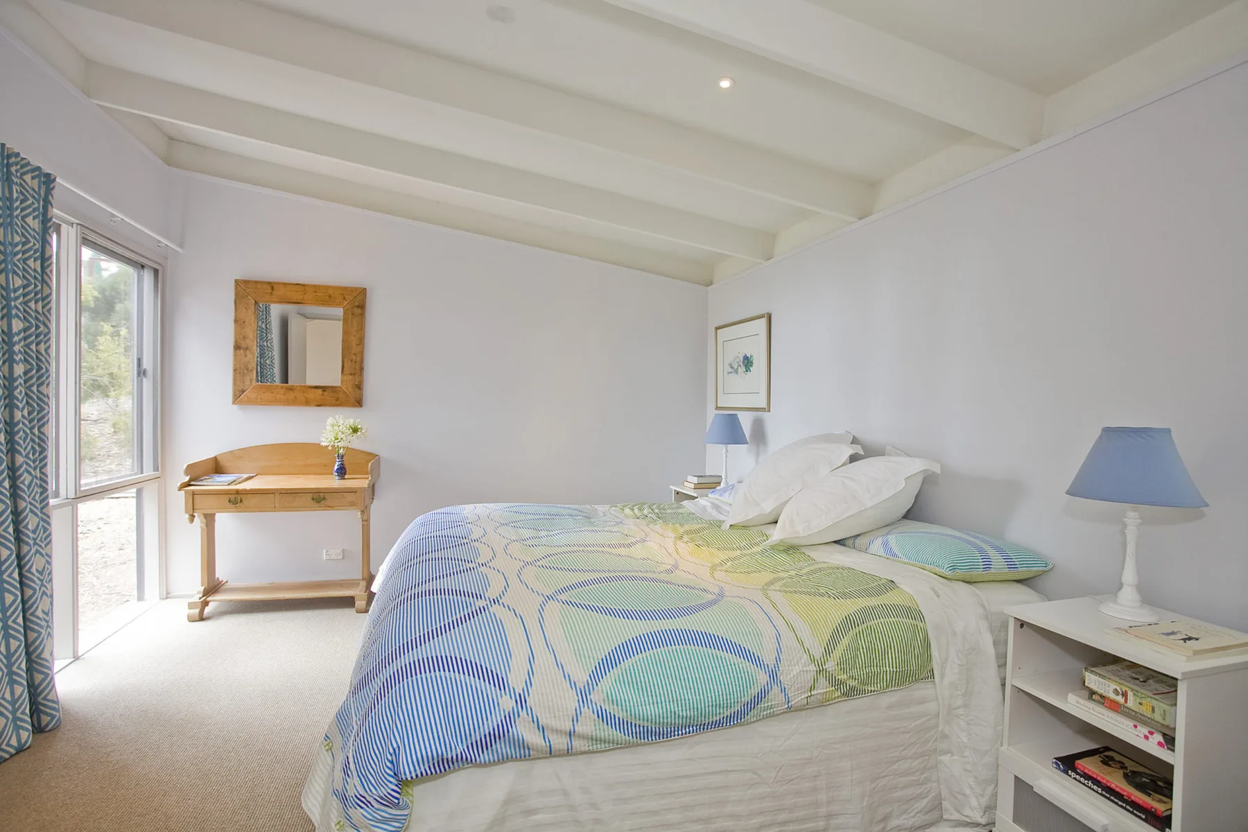 A bright bedroom with a patterned bedspread and a desk beside the window.