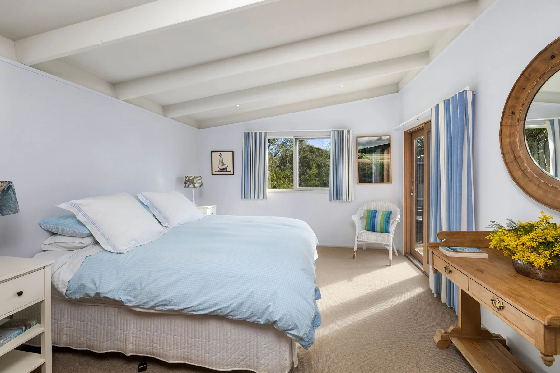 A bright bedroom with a bed, windows, and a wooden dresser.