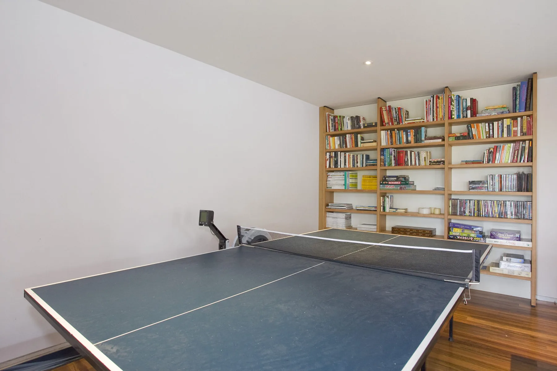 A table tennis table sits in front of a wall of bookshelves.