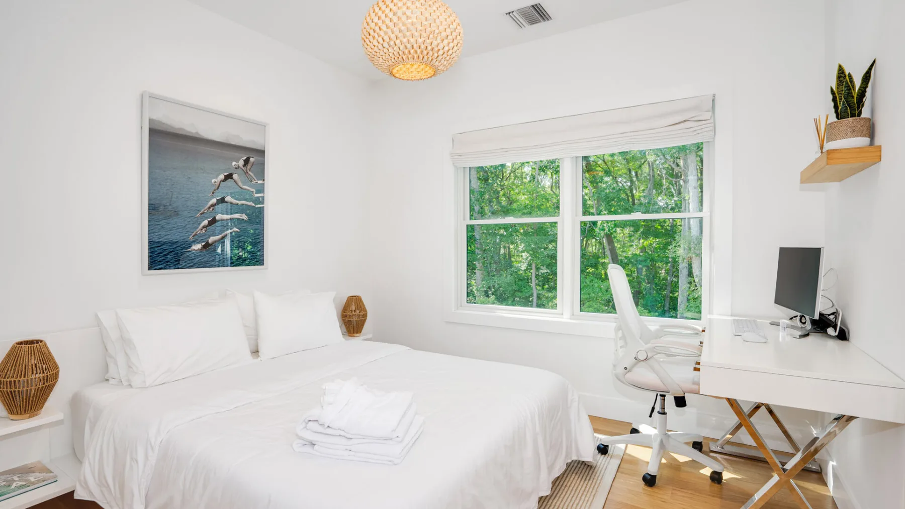 A bright bedroom with a white bed and a window overlooking greenery.
