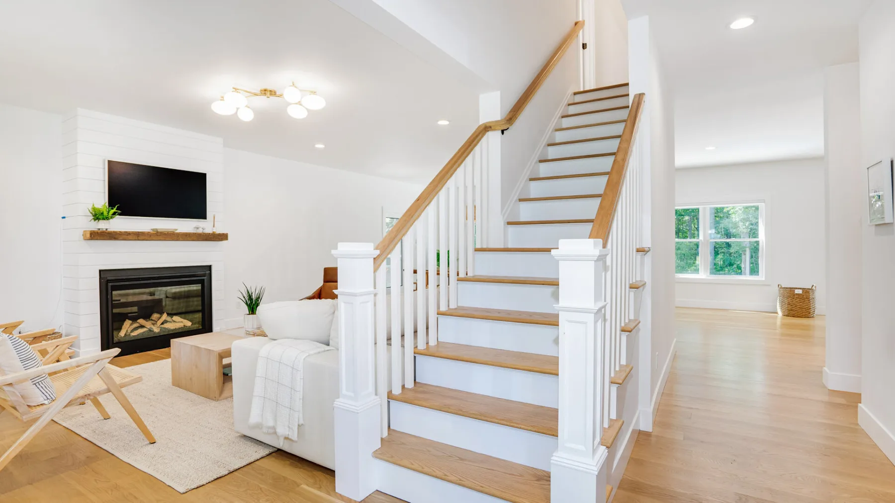 A bright living room with a fireplace, seating, and a staircase.
