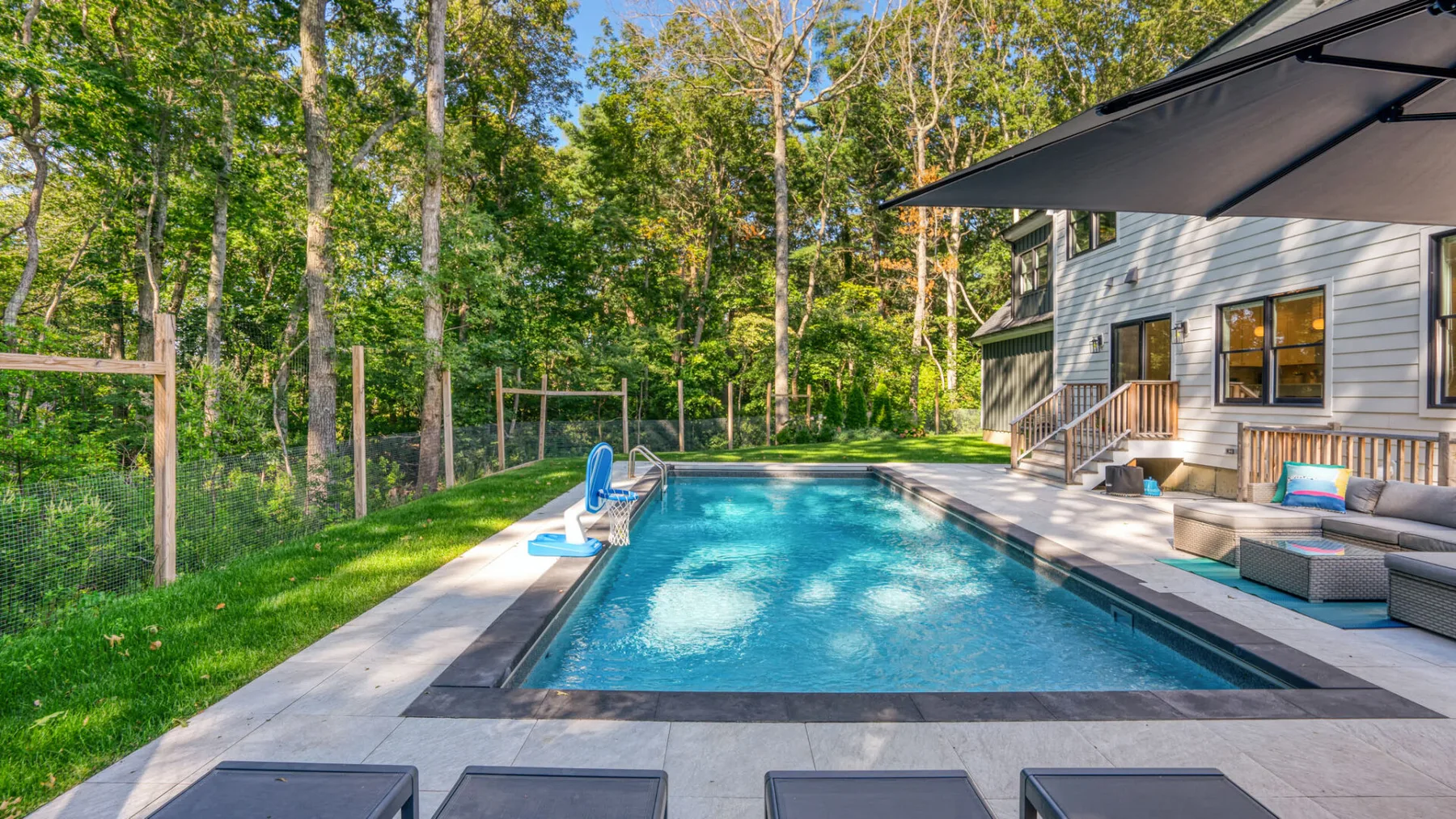 An outdoor swimming pool beside a house, with lounge seating under a shaded patio.
