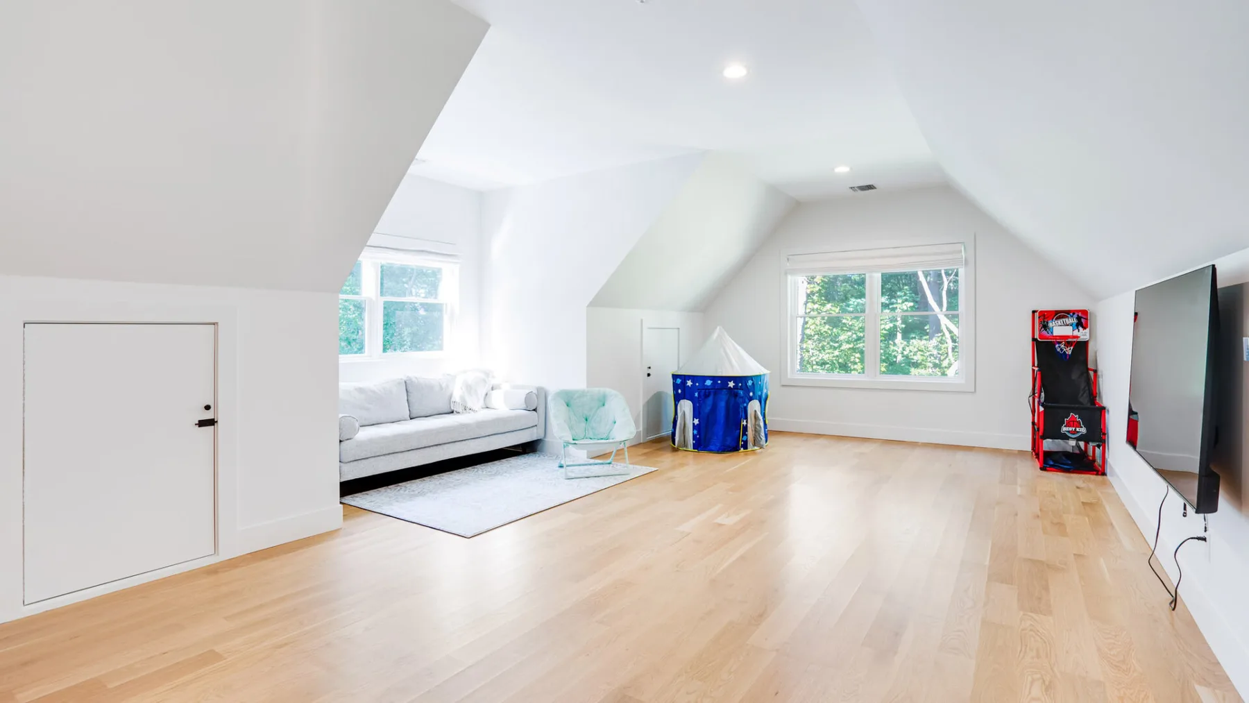 A bright attic living area with white seating, windows, and a wooden floor.