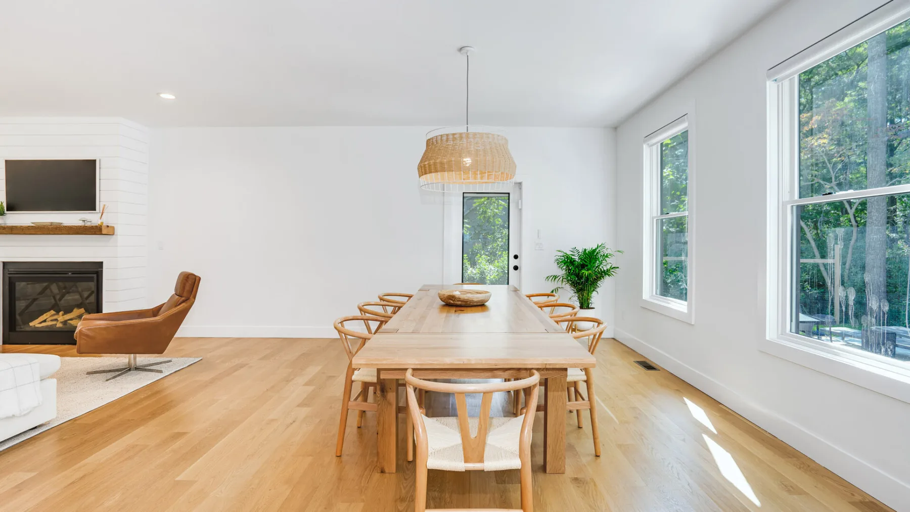A bright dining area with a long wooden table beside large windows.